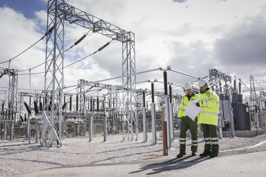 Two engineers in high-visibility clothing reviewing plans at an electricity substation
